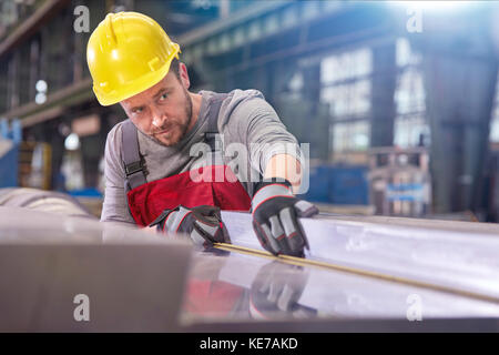 Fokussierter männlicher Arbeiter, der Stahl in der Fabrik untersucht Stockfoto