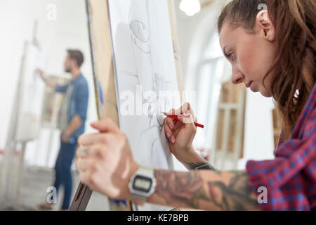 Fokussierte Künstlerin mit Tattoo Skizzieren an Staffelei in der Kunst Klasse Studio Stockfoto
