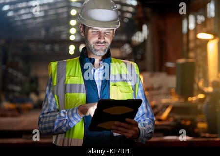 Männlicher Ingenieur, der an glühenden digitalen Tablette in dunkler Fabrik arbeitet Stockfoto