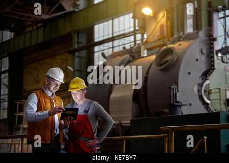 Männlicher Ingenieur und Arbeiter mit digitalem Tablet in dunkler Fabrik Stockfoto