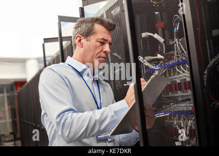 Männlicher IT-Techniker schreibt auf Zwischenablage an der Zentrale im Server Zimmer Stockfoto