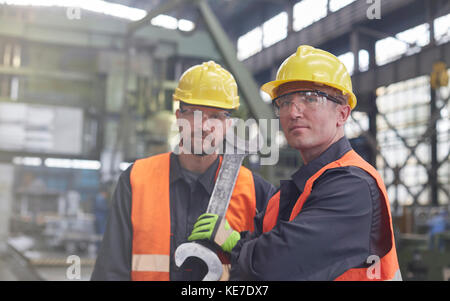 Portrait selbstbewusste, robuste männliche Arbeiter mit großem Schraubenschlüssel in der Fabrik Stockfoto