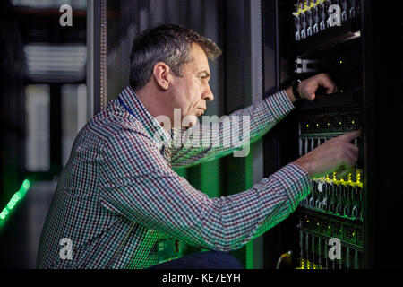 Fokussierter männlicher IT-Techniker, der an der Zentrale in einem dunklen Server arbeitet Zimmer Stockfoto