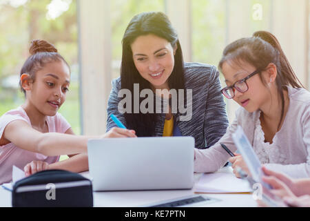 Lehrerin und Schülerinnen erforschen am Laptop in der Bibliothek