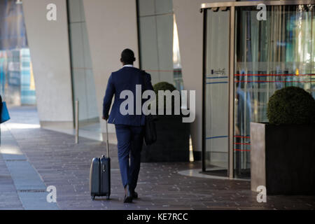 Schwarzer Geschäftsmann in blauem Anzug mit Trolley-Koffer beim Verlassen des Hotels, Drehtür Eingang Radisson Blu Hotel, Glasgow Stockfoto