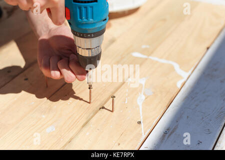 Der Mann dreht die Schrauben in die Bretter mit einem Schraubendreher. Stockfoto