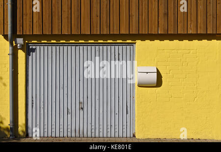 Yellow Brick Wall mit Garagentor, Briefkasten, Downspout und braune Holzvertäfelung im zweiten Stock Stockfoto