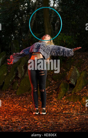 Mädchen rollt eine Hoop über ihre Brust, Hoop in der Luft ausgesetzt ist, die Arme ausgestreckt, bis suchen, mit kreativen Beleuchtung im Wald. Stockfoto