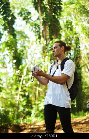 Ein junger Mann steht auf einem Trail trägt einen Rucksack und ein Bild mit einer Kamera, während auf einer Wanderung, Hawaii, Vereinigte Staaten von Amerika Stockfoto