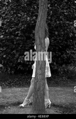 Frau versteckt sich hinter einem Baum Stockfoto