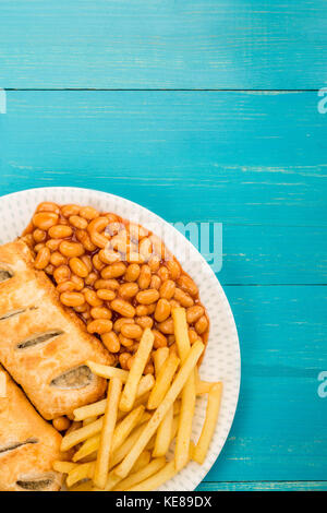 Würstchen, Brötchen mit Baked Beans Chips und Pommes frites auf einem blauen Hintergrund mit Kopie Raum Stockfoto