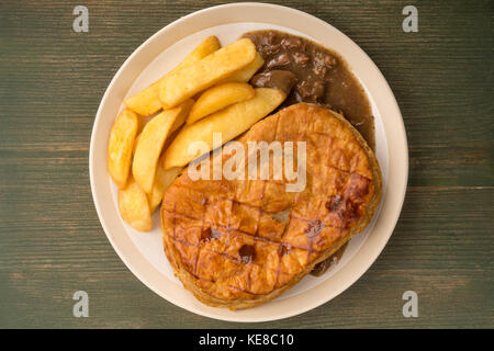 Rindfleisch Steak pie mit einem Blätterteig Kruste oben und Chips auf einem grünen Holz- Hintergrund mit Kopie Raum Stockfoto