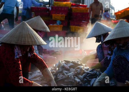 Nicht identifizierte die Menschen vor Ort auf einem Marktplatz arbeiten, Frau ist selektive Fisch und Mensch ist Korb aus Schiff am Strand tragen. Sunflare mit Unscharf Stockfoto