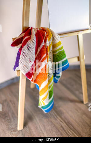 Ein Fragment eines handgefertigte Mehrfarbige gestrickter Schal, der in ein Haus innen auf einer Staffelei. Farben des Regenbogens. Das Konzept der Wohnkomfort, Handarbeit, kni Stockfoto