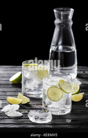 Selektiver Fokus Komposition mit Gin und Tonic Cocktail mit Zitrusfrüchten auf hölzernen Tisch serviert mit Stücken Eis Stockfoto
