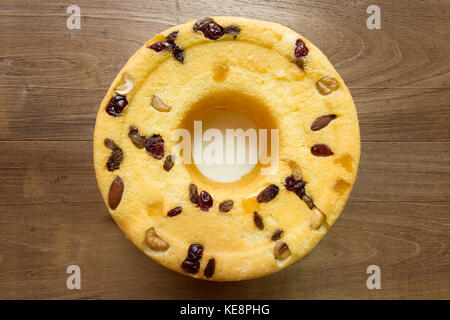 Hausgemachter Baumwollkuchen, Mischung aus Mandelfrüchten, Cashewnüssen, Preiselbeeren, getrockneten Mangos, grünen Rosinen, auf weißem Teller, auf rustikalem Holztisch, flacher Laie Stockfoto
