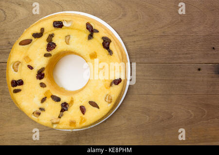 Hausgemachter Baumwollkuchen, Mischung aus Mandelfrüchten, Cashewnüssen, Preiselbeeren, getrockneten Mangos, grünen Rosinen, auf weißem Teller, auf rustikalem Holztisch, flacher Laie Stockfoto