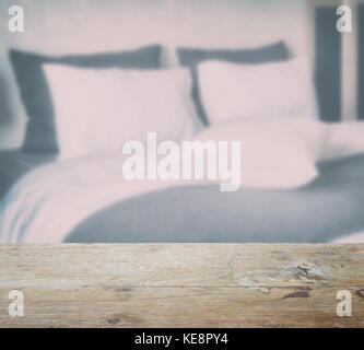 Holz- Tischplatte und Unschärfe der saubere Bettwäsche mit King size Bett im modernen Schlafzimmer Innenraum Stockfoto