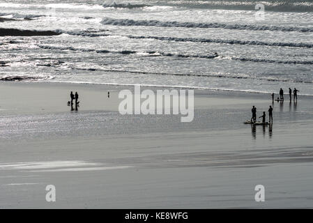 Personen Silhouette gegen einen Sandstrand und Wellen aufgrund der späten Nachmittagssonne Stockfoto