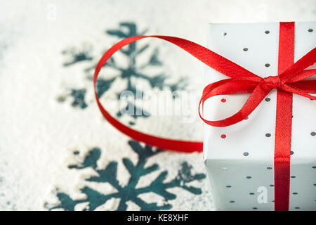 Elegante Geschenkbox in Grau Silber Papier umhüllt mit Polka Dots red ribbon auf verschneiten Hintergrund mit Schneeflocken. Weihnachten neue Jahre präsentiert s Shopping Stockfoto