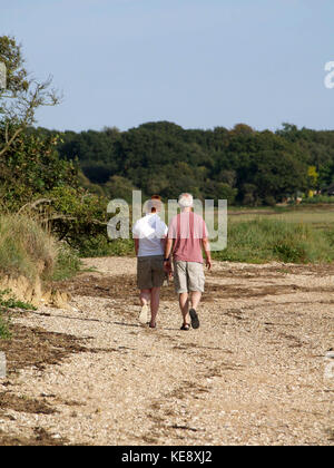 Ältere Paare, die auf dem Fußweg im Hafen von Bosham, Hampshire, England, Großbritannien spazieren Stockfoto