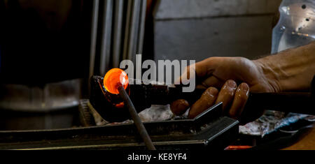 Nahaufnahme des traditionellen Handwerkers bei der Arbeit in Glasbläserei. Hand greifende Werkzeuge des Mannes, die glühendes geschmolzenes Glas Formen. Großbritannien Glasbläserkunst Stockfoto