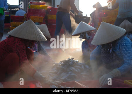 Nicht identifizierte die Menschen vor Ort auf einem Marktplatz arbeiten, Frau ist selektive Fisch und Mensch ist Korb aus Schiff am Strand tragen. Sunflare mit Unscharf Stockfoto