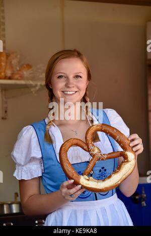 Schöne junge Frau mit geflochtenem Haar zu tragen traditionelle Schweizer dirdl Kleid halten Frische grosse Brezel am Oktoberfest in New Glarus, Wisconsin, USA Stockfoto