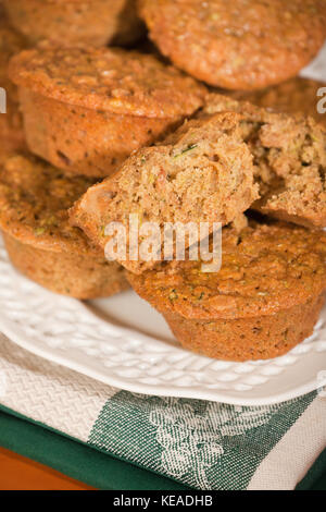 Zucchini Muffins, mit einem Schnitt in der Hälfte, auf einem weißen Keramikplatte ruht auf Kaffee Handtücher auf ein Holz Tisch gestapelt Stockfoto