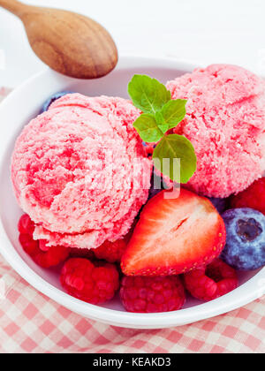 Nahaufnahme Eis mixed berry Früchte Himbeere, Heidelbeere, Erdbeere und Pfefferminze Blätter setup in Weiß Schüssel auf weißem Holz- Hintergrund. Sommer ein Stockfoto