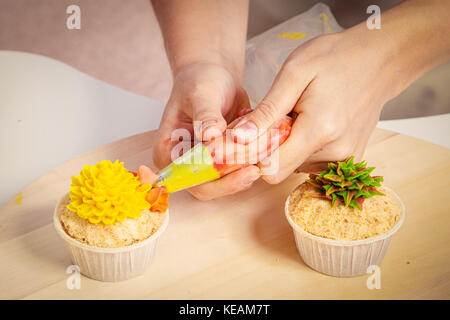 Eine Nahaufnahme der Konditor Frau schmückt mit Gebäck Spritze eine Cupcake aus natürlichen Produkten mit einem süßen Creme von gelber Farbe von Gre gemacht Stockfoto