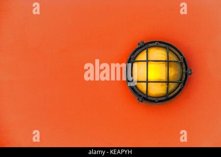 Gelbe Stirnwand Licht (ship Deck Lampe) durch einen verrosteten Rahmen mit einem rot-orange Farbe Holz wand hintergrund Feste umgeben. Stockfoto