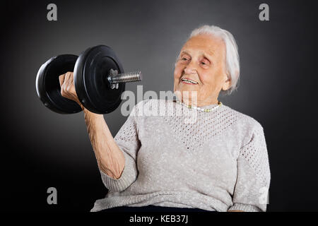 Gerne ältere Frau, Übung mit hantel über grauer Hintergrund Stockfoto