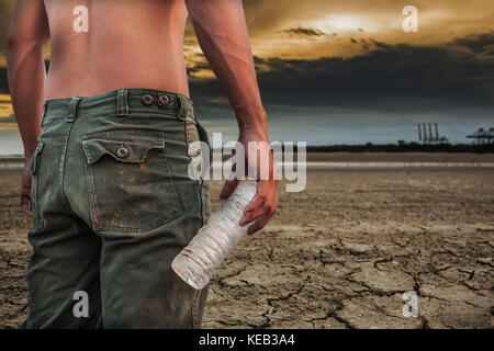 Mann hält eine Flasche Wasser Land auf den Boden trocknen Risse Stockfoto