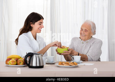 Ältere Frau mit Cookie zu pflegen, während Sie Kaffee Stockfoto