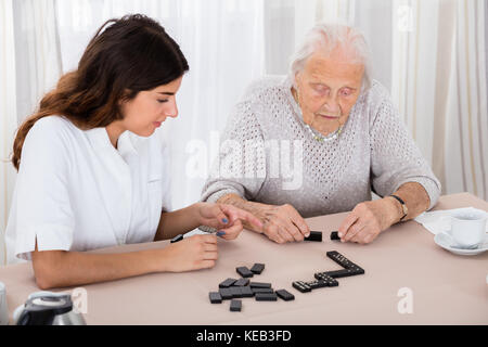 Ältere Frau spielen Domino Spiel auf Tabelle mit ihrer Amme im Krankenhaus Stockfoto