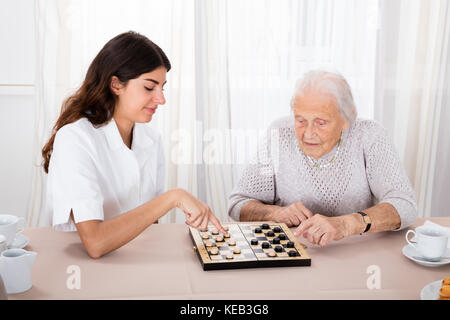 Ältere Frau spielen checkers Spiel mit junge Krankenschwester auf Tisch Stockfoto