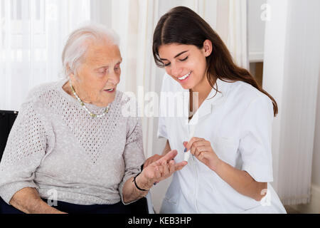 Gerne Ärztin Kontrolle der Blutzuckerspiegel von älteren Patienten mit glucometer in Klinik Stockfoto