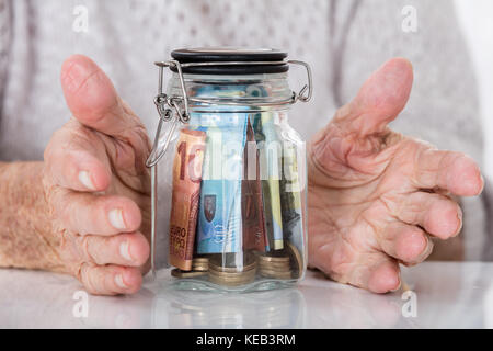 In der Nähe der älteren Frau, die schützende Hand Glas Glas Geld Stockfoto