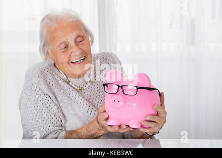 Gerne ältere Frau mit Sparschwein zu Hause Stockfoto