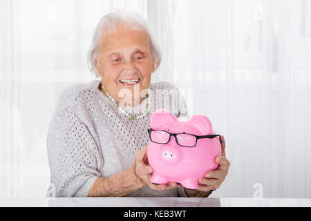 Gerne ältere Frau mit Sparschwein zu Hause Stockfoto