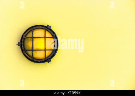 Gelbe Stirnwand Licht (ship Deck Lampe) durch einen verrosteten Rahmen ein Gemaltes Licht gelb Pastell Holz Wand umgeben. Stockfoto