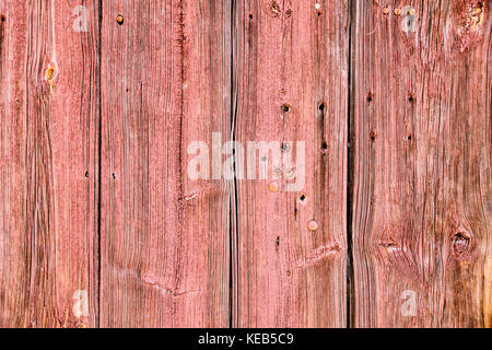 Alten grunge und verwitterte rot Holz- wandplanken Textur mit rostigen Nägeln und Bohrungen durch die Elemente im Freien. Stockfoto