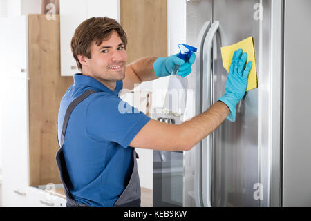 Junger Mann Reinigung Edelstahl Kühlschrank mit rag und Flasche Spray in der Küche Stockfoto