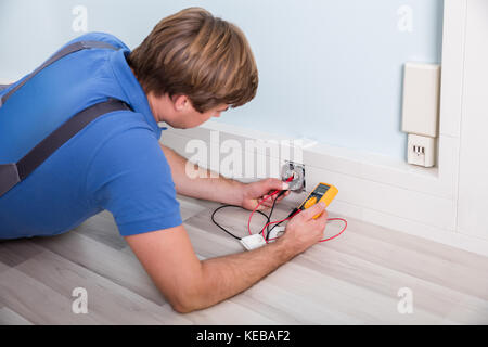 Elektriker prüfen Steckdose Spannung mit Hilfe eines Multimeters mit einer Wandhalterung Stockfoto