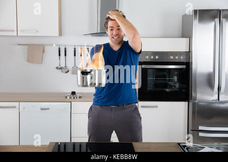 Junge überrascht Mann hält Utensil auf Feuer in der Küche Stockfoto