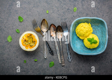 Die Zusammensetzung von Speiseeis Passionsfrucht Aroma in vintage Schüssel setup auf dunklem Stein Hintergrund. Passionsfrüchte mit Pfeffer Minze und Utensilien. Stockfoto