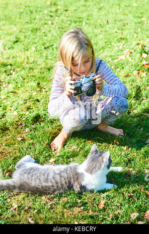 Kind Mädchen Fotografieren einer Katze, die auf dem Gras draussen im Garten. Stockfoto