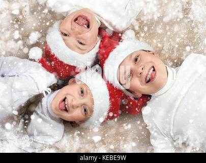 Glückliches Kind zusammen liegen auf Holz- Hintergrund, in weihnachten santa hut gekleidet und Spaß haben, Winterurlaub Konzept, Schnee, Dekoration Stockfoto