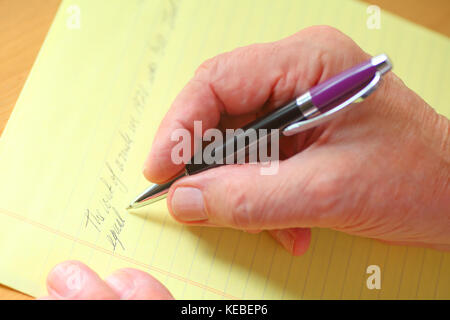 Ältere Mann schreibt in Schreibschrift auf eine Regelfläche gelb Block Papier Stockfoto